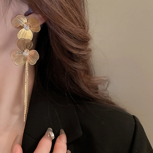 Détail de boucles d'oreilles fleurs dorées avec pompons et cristaux sur un mannequin