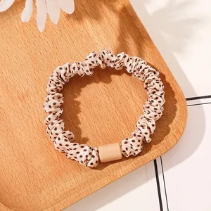 Close-up of leopard print scrunchie with matte bead detail on a wooden tray with flowers