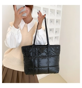 Detailed view of black quilted down tote bag with long handles worn on shoulder