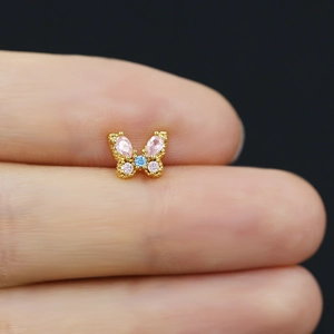 Macro shot of a tiny gold butterfly stud earring with pink and blue zircons between fingers