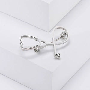 Detailed view of silver metal stethoscope brooch on a white geometric display stand