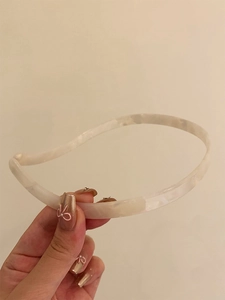 Close-up of a minimalist cream acetate headband with marble texture and polished finish