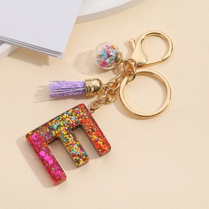 Close-up of resin letter E keychain with colorful sequins and purple tassel decoration