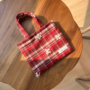 Détail du sac à main en laine à carreaux rouges avec nœud au crochet et étiquette tissée