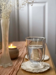 Close-up of a double-walled glass cup on a handcrafted woven coaster with fringe details