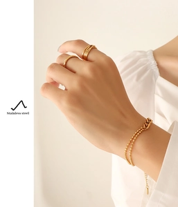 Close-up of dual-layer gold beaded bracelet and stacked rings on a female hand