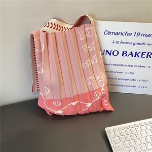 Detail of pink pleated knit handbag with white abstract patterns and striped strap
