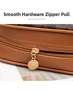 Detail shot of golden metal zipper pull on a brown checkered leather crossbody bag