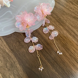 Macro detail of pink acrylic flower earrings with long golden chain tassels on a base