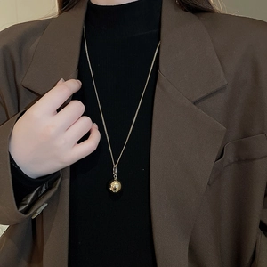 Detailed close-up of a gold ball pendant necklace on a model wearing a dark blazer