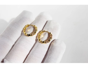 Detail showing gold-plated bamboo hoop earrings with white zircon on a hand