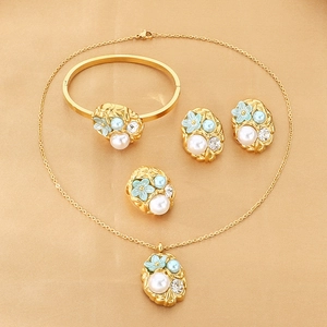Macro view of gold jewelry set featuring light blue enamel flowers and white pearls