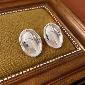 Detail of silver liquid metal style irregular earrings on green velvet surface