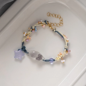 Handmade woven bracelet featuring orange beads, star charm, and cat beads on a ceramic tray