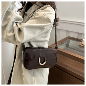 Detail of dark brown patent leather bag with gold buckle on a model's shoulder