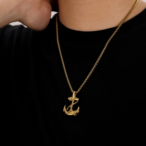 Close-up of a gold anchor pendant necklace worn by a man against a black t-shirt background