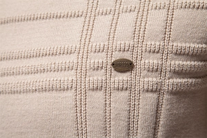 Detailed macro view of the 3D textured knit fabric and metal logo badge on beige sweater