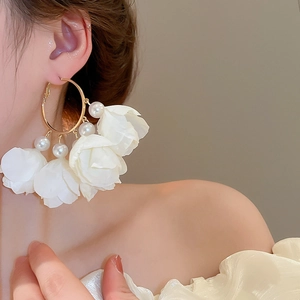 Close-up of white fabric flower earrings with gold hoop and pearls worn by a model