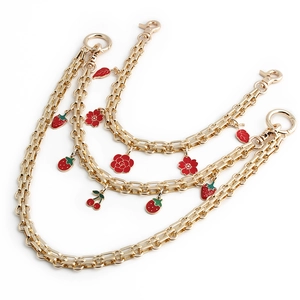 Three-layer gold metal bag chain with red strawberry and cherry charms on white background