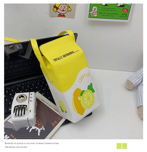Close-up of lemon juice box shaped crossbody bag on a desk with laptop and magazine