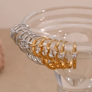 Detail of gold and silver earrings with zircon charms on a transparent glass edge