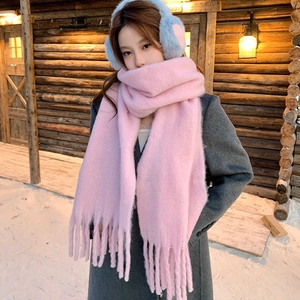 Woman in stylish pink mohair tassel scarf and blue plush earmuffs in winter snow