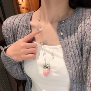 Detail of pink strawberry pendant necklace with pearls worn on grey knit sweater
