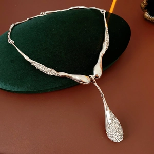 Détail du collier goutte en argent scintillant sur un coussin en velours vert