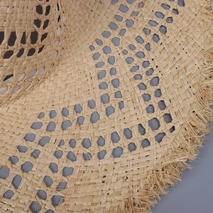 Detailed close-up of beige raffia sun hat showing hollow weave pattern and fringe edge