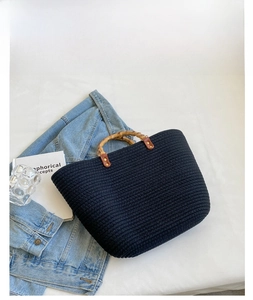 Detail of woven black tote bag with bamboo handle and golden metal rivets on white fabric