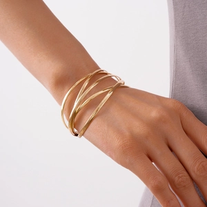 Close-up of golden multi-layered crisscross bangle on wrist with minimalist metallic design