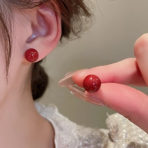 Close-up of elegant red spherical stud earrings showing polished finish on the ear