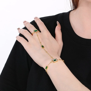 Detail of 18k gold slave bracelet featuring green crystals on ring and chain