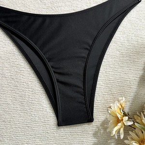 Flat lay of black high-cut bikini bottoms on textured fabric with decorative dried flowers