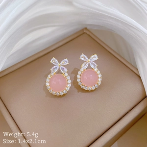 Detailed close-up of bowknot pink earrings with zircons on elegant silk background