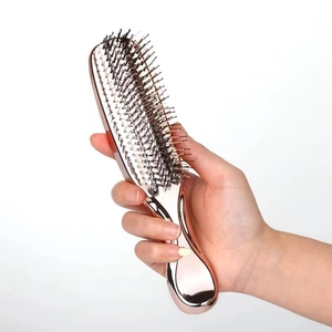 Close-up of a hand holding a rose gold electroplated hairbrush with black bristles