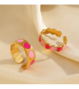 Dettaglio di anelli in titanio placcato oro 18K con cuori in smalto rosa su seta bianca