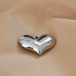 Close-up of a silver heart-shaped pendant with polished mirror finish on soft beige fabric