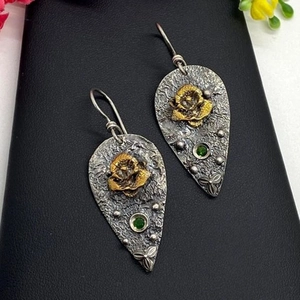 Vintage teardrop earrings with gold rose detail and green gemstone on black background