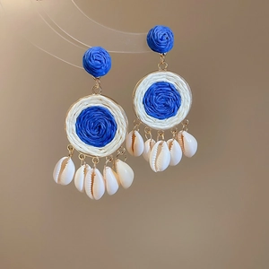 Close-up of Bohemian raffia woven earrings with blue beads and natural sea shell tassels