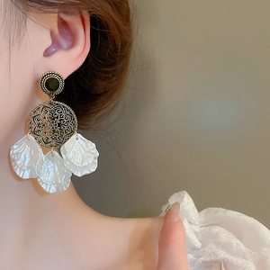 Gros plan de boucles d'oreilles vintage dorées à glands et pétales blancs sur modèle