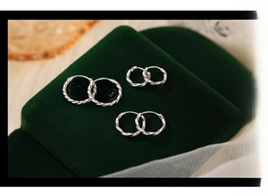 Three pairs of twisted s925 silver hoop earrings in different sizes on green velvet