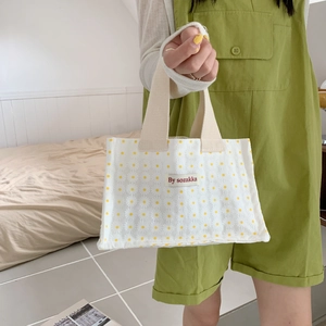 Close-up of a white canvas lunch bag featuring small yellow daisy prints and a brand label
