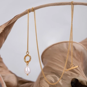 Macro shot of gold necklace with baroque pearl pendant and T-bar toggle clasp on a leaf