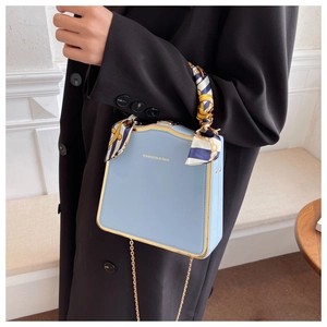 Close-up of light blue box bag with gold metal frame and silk scarf wrapped handle