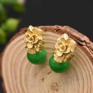 Golden flower earrings with green jade beads on wood background, retro nature style