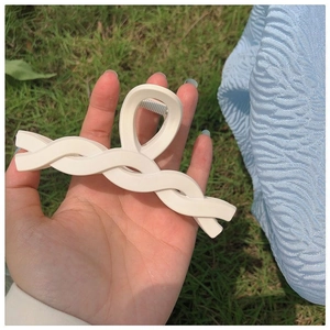 Close-up of a beige twisted hair claw clip held by hand against a green grass background