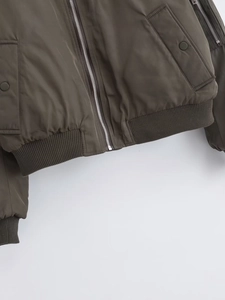 Detail of a bomber jacket showing silver zipper, snap pockets and ribbed knit hemline