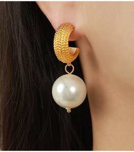 Macro detail of gold C-shape hoop earrings with chain texture and large pearl drops