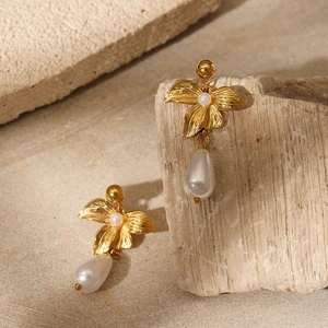 3D golden flower earrings with pearl drops on a natural stone textured background